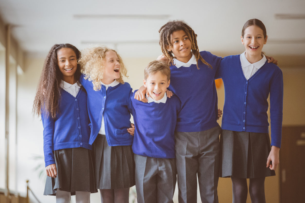 Five children in blue sweaters, smiling and standing together indoors.