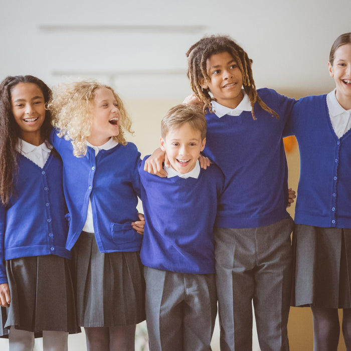 Five children in blue sweaters, smiling and standing together indoors.